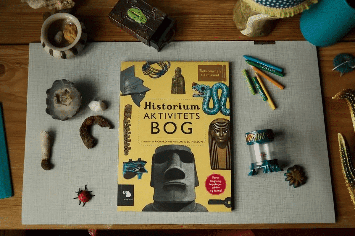 Opgavebøger. Aktivitetsbogen Historium fra forlaget mammut ligger på et bord omgivet af pynte ting.