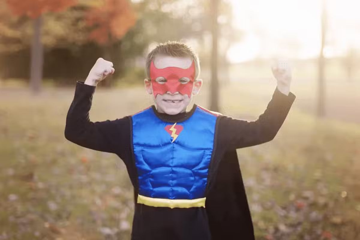 Superhelte kostume. En sej dreng spænder op i musklerne, mens han er klædt i et superhelte kostume. Han befinder sig udenfor.