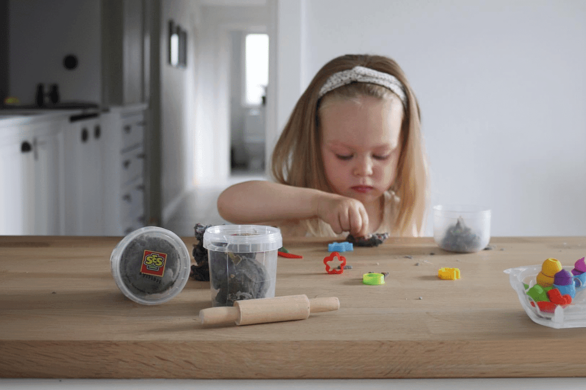 En pige sidder ved et bord og leger med modellervoks.