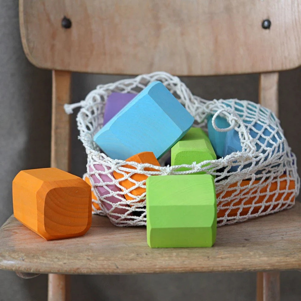 Grimms Træklodser i Net i en kurv på en stol med farverige træklodser i blå, grøn, orange og lilla.